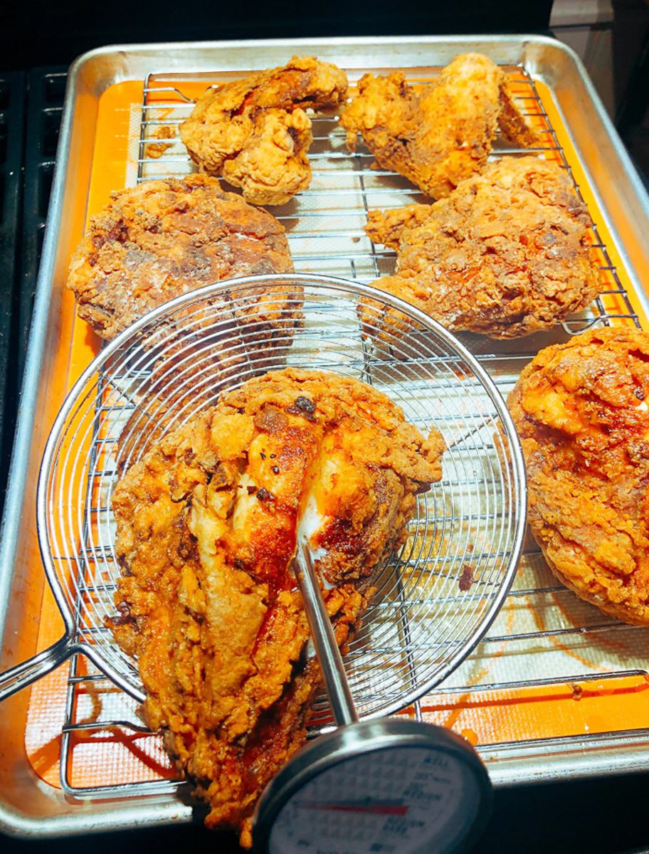 A candy thermometer in hot fried chicken in a metal basket on a baking sheet this makes it the crispiest fried chicken! 