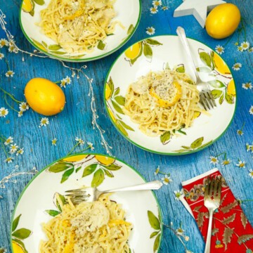three lemon plates with lemon pasta and chicken on top with sterling silver forks and lemons