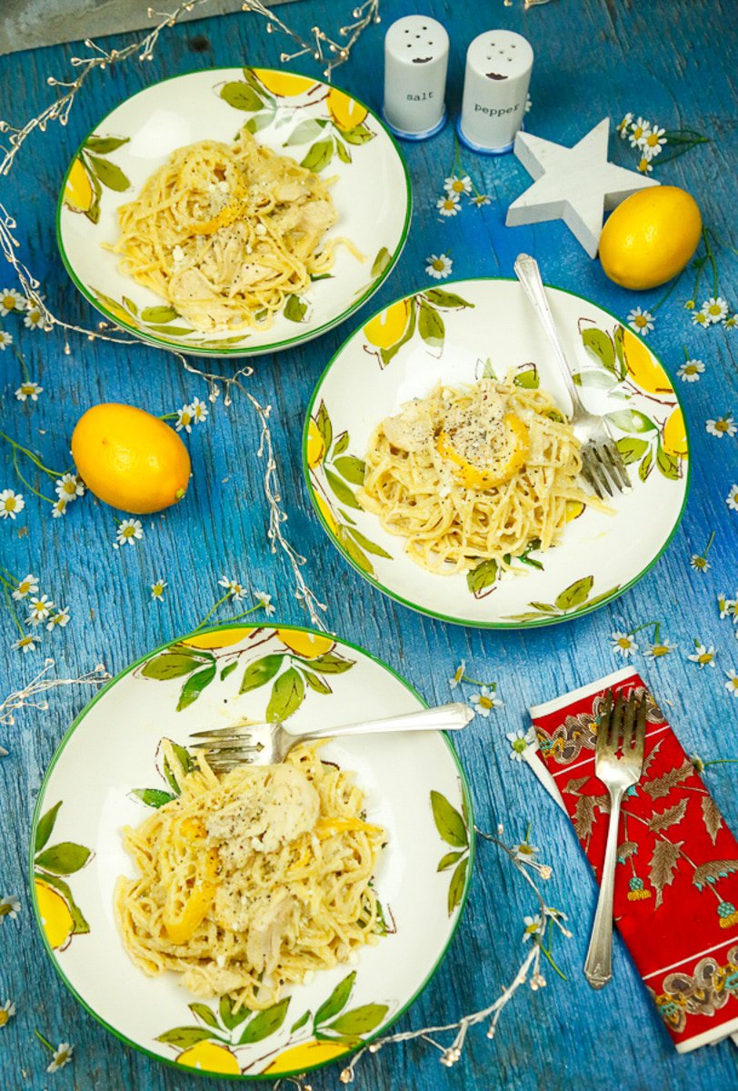 three lemon plates with lemon pasta and chicken on top with sterling  silver forks and lemons 