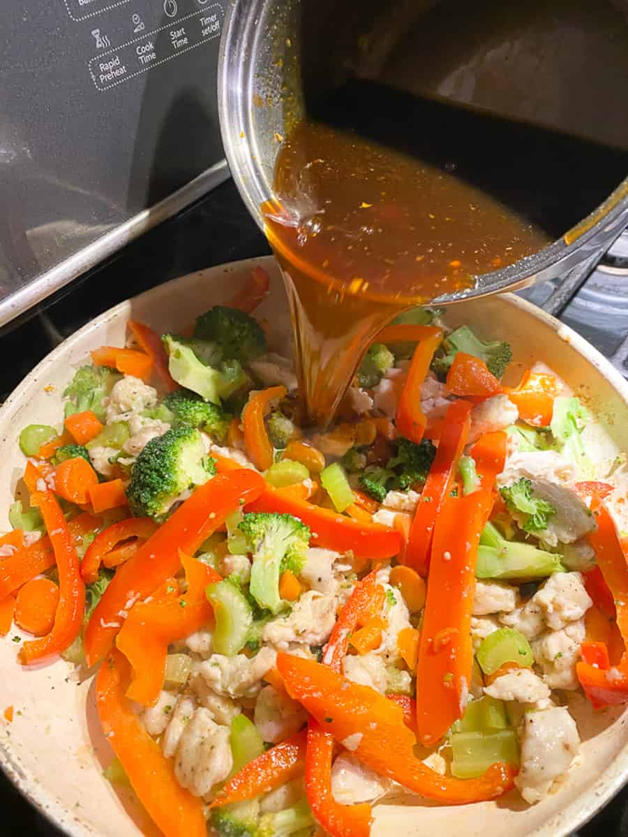 orange sauce being poured over the chicken and veggies for healthy orange chicken recipe