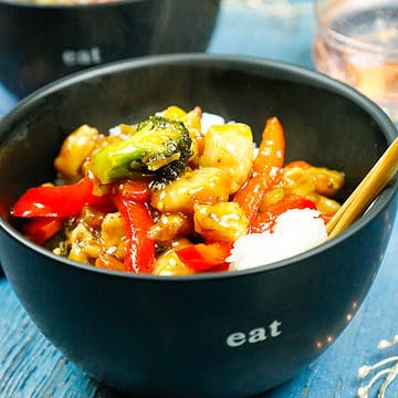 Orange chicken and veggies served over Jasmin rice in black bowls that say eat with chop sticks