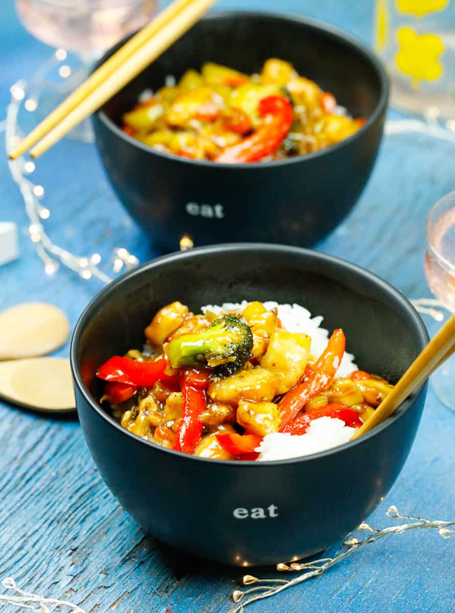 bowls of healthy orange chicken and vegetables over rice in black bowls with chop sticks