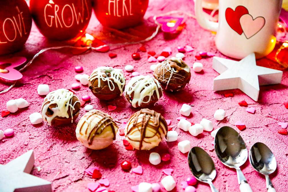 Valentine's Hot Chocolate Bombs on a pink backdrop with Rae Dunn spoons 