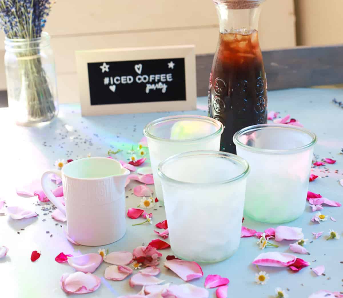 three frozen glass weck jars with a tall pitcher of iced coffee and cream with lavender flowers and rose petals 
