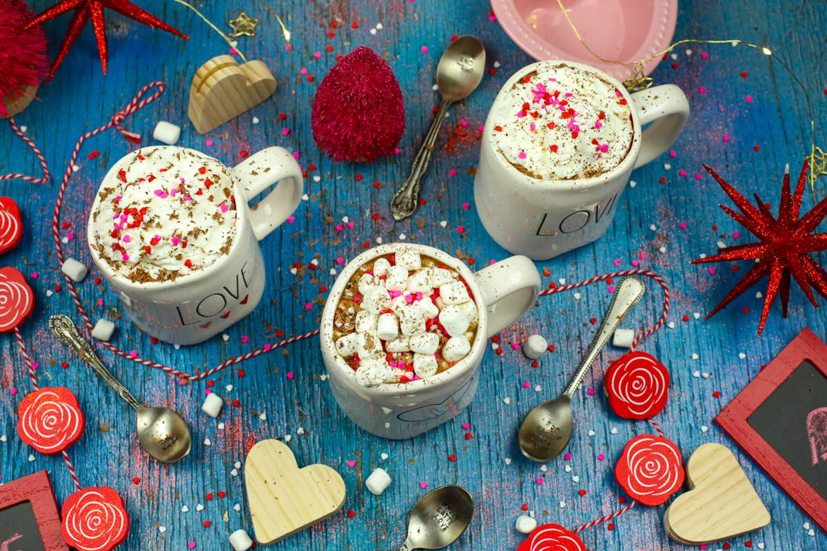Three Rae Dunn mugs filled with hot chocolate and topped with homemade whipped cream and, marshmallows, and sprinkles 