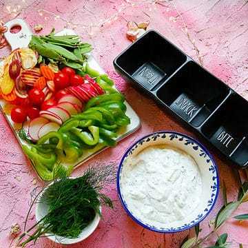 Ranch dressing with a black dip jar with veggies and fresh herbs