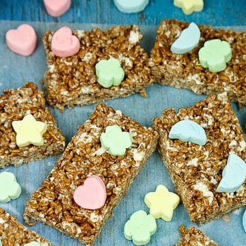 Chocolate rice krispies squares with colored marshmallows on them on a blue backdrop