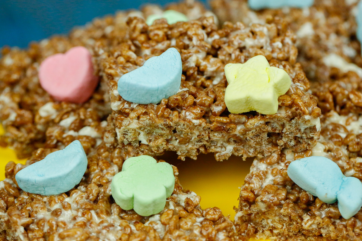 a stack of chocolate rice krispies with lucky charm marshmallows on a yellow cake stand 