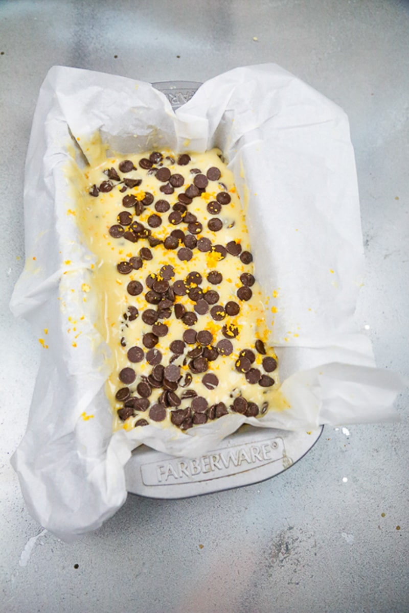 Orange cake batter with chocolate chips in a loaf pan with wax paper 