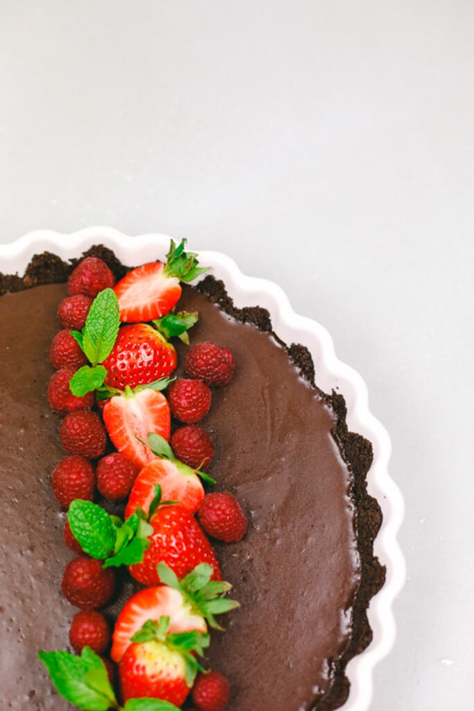 A chocolate coffee ganache tart with fresh raspberries and strawberries made with a chocolate graham cracker crust in an Ikea tart plate