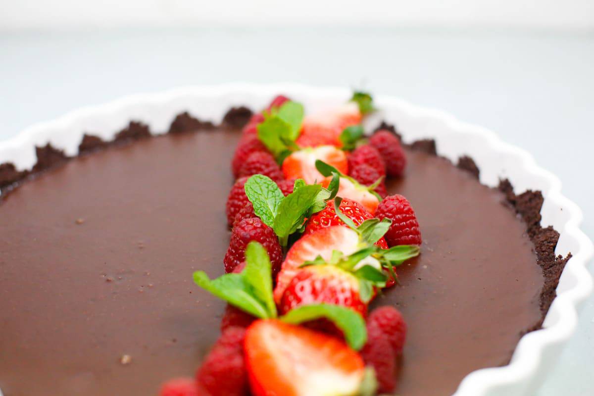 A beautiful chocolate coffee ganache tart topped with fresh berries and sprigs of mint 