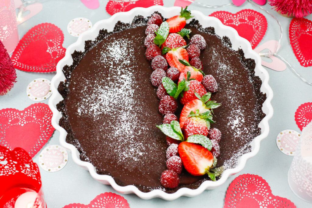 A chocolate coffee ganache tart with fresh berries and powered sugar with a chocolate crust 