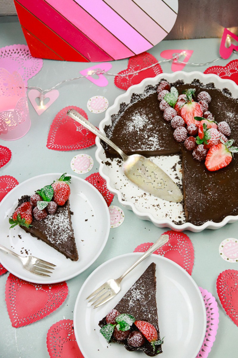 Chocolate cake slices sitting on white plates with Valentine's paper mache and topped with fresh berries and mint with a light dusting of powered sugar 