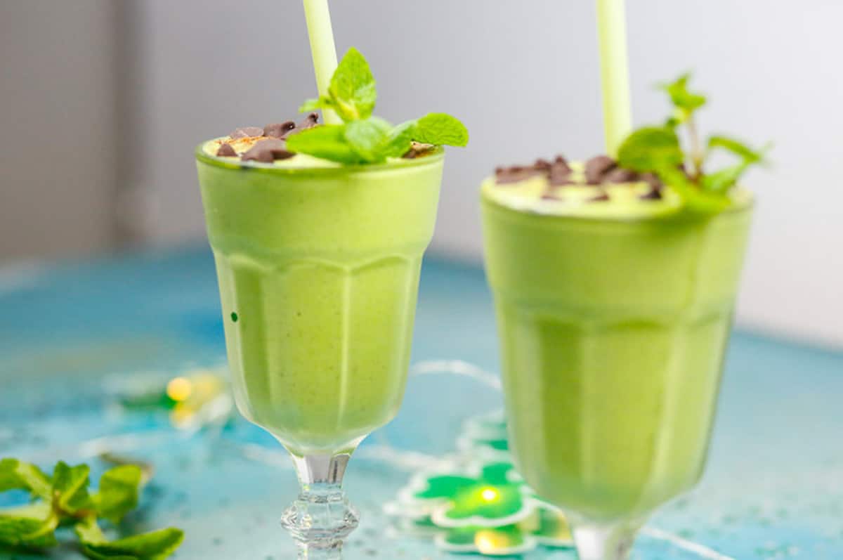two glasses on a table with a blue backdrop and shamrocks of green mint milkshake