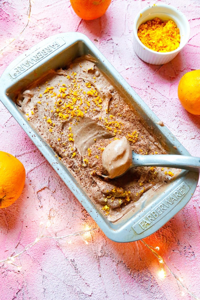 Chocolate orange ice cream in a metal cake pan on a pink backdrop with fair lights and oranges 