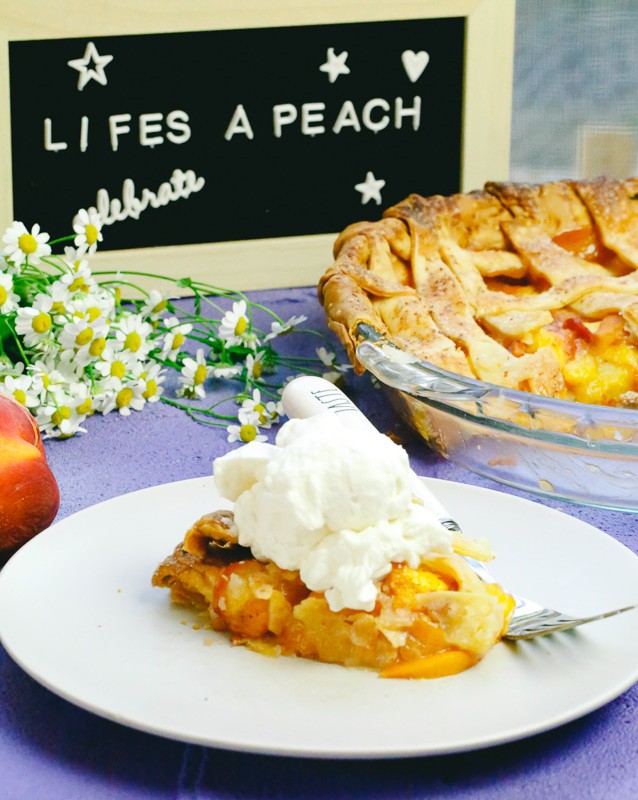 Homemade peach pie made with fresh peaches and honey on a plate with a fork next to a life's a peach sign