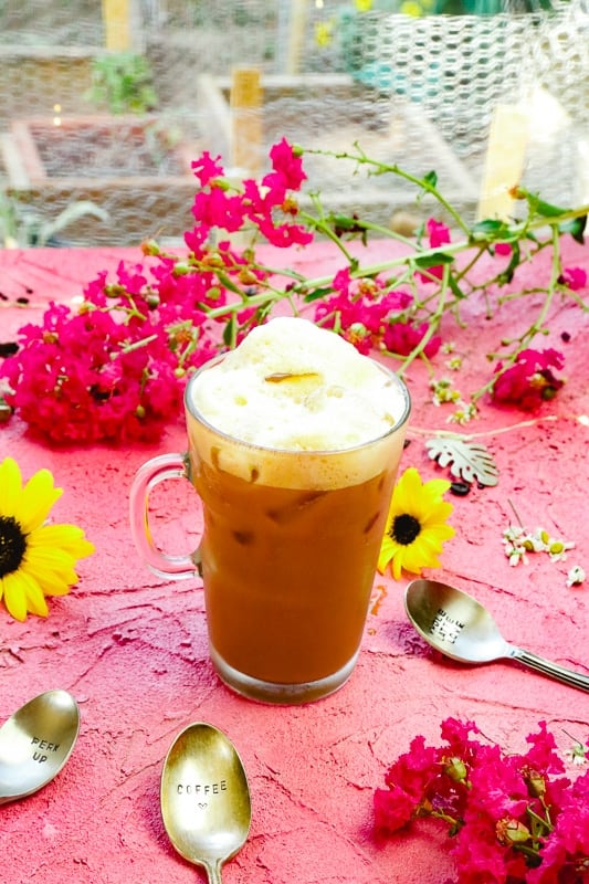 Glass filled with foam and iced coffee shakerato with Italian espresso and sweet milk next to sunflowers