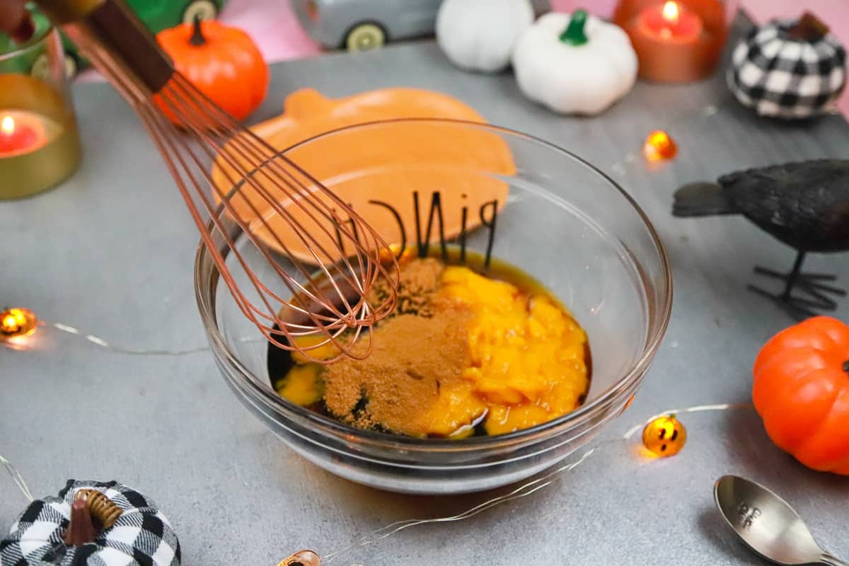a whisk combining ingredients of pumpkin puree pumpkin spice molasses and maple syrup 