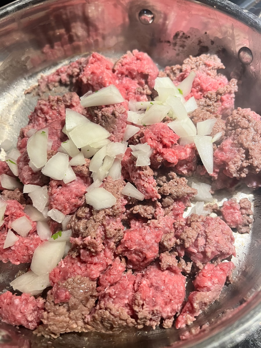 ground beef and white onion cooking in a pan on the oven 