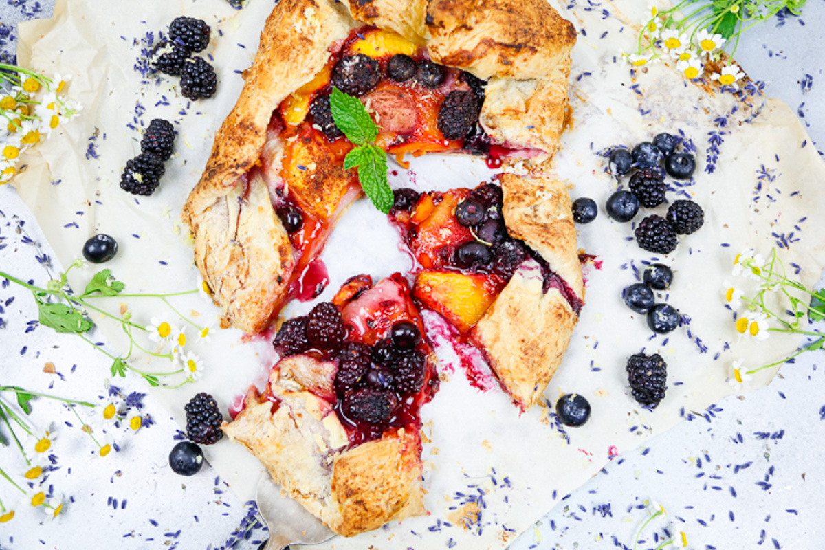 puff pastry peach galette topped with blackberries, blueberries, mint sprigs and a metal pie cutter