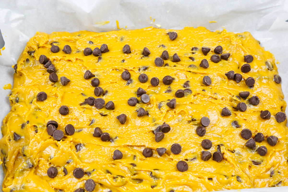 pumpkin brownie batter topped with chocolate chips in a tray with wax paper for pumpkin brownies healthy 