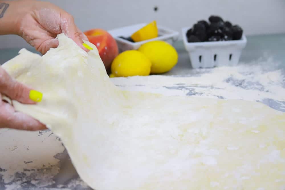 rolled out puff pastry dough with trays of fruit in the background