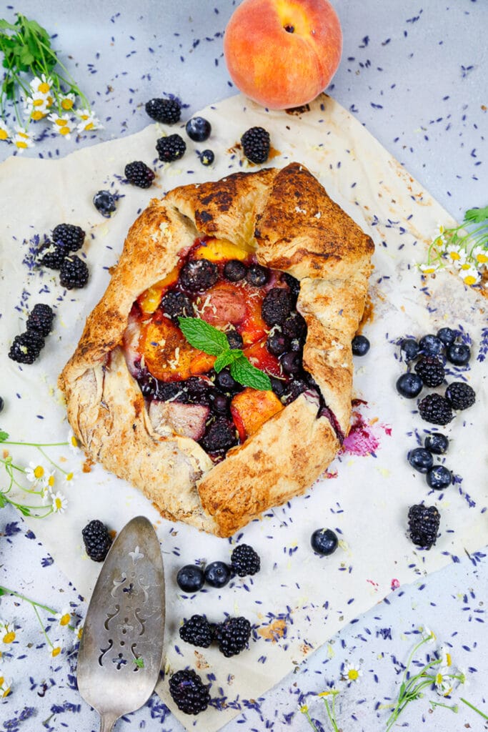 flat lay of bake stone fruit galette with mint and a peach sitting on top of the baked galette