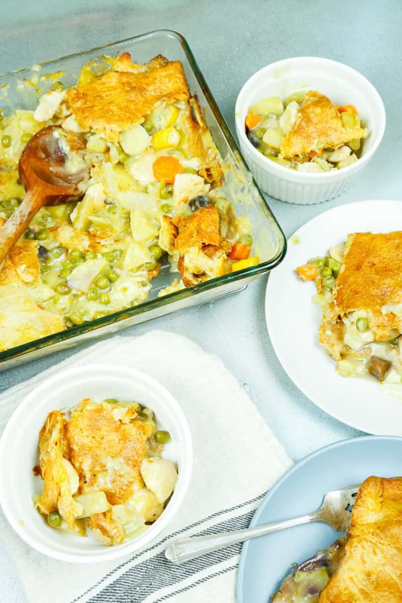 Chicken Pot pie with puff pastry in a casserole dish with slices of chicken pot pie on white plates 