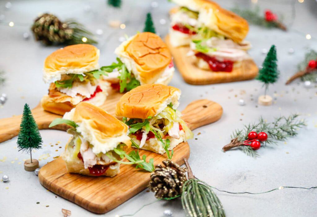 stacked turkey sandwiches on mini cutting boards with layers of turkey, arugula, cranberry sauce, for leftover turkey sliders 