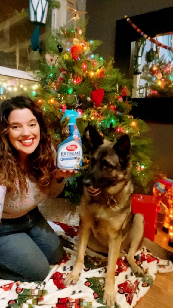 girl in front of Christmas tree holding simple solutions stain remover with German Shepherd