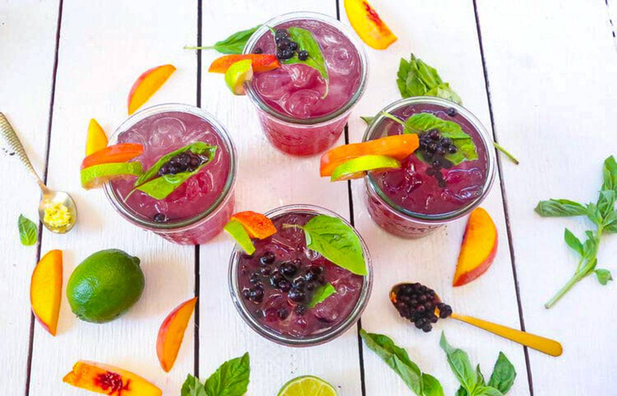 basil, limes, peaches, frozen blueberries, and peaches in glasses with gold spoons and ice 