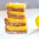 a stack of lemon bars on a white wood backdrop with a lemon sitting next to them