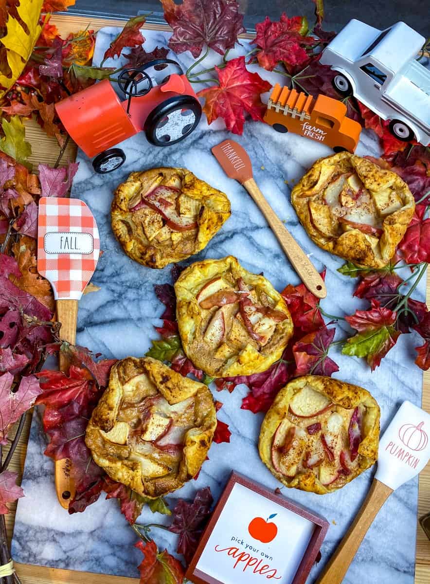 mini apple pies with pear and apple and baking spoons with a tractor, orange truck and leaves on a marble back drop 