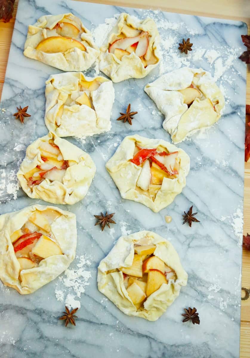 open faced apple pies on a marbled flour surface with star anise 