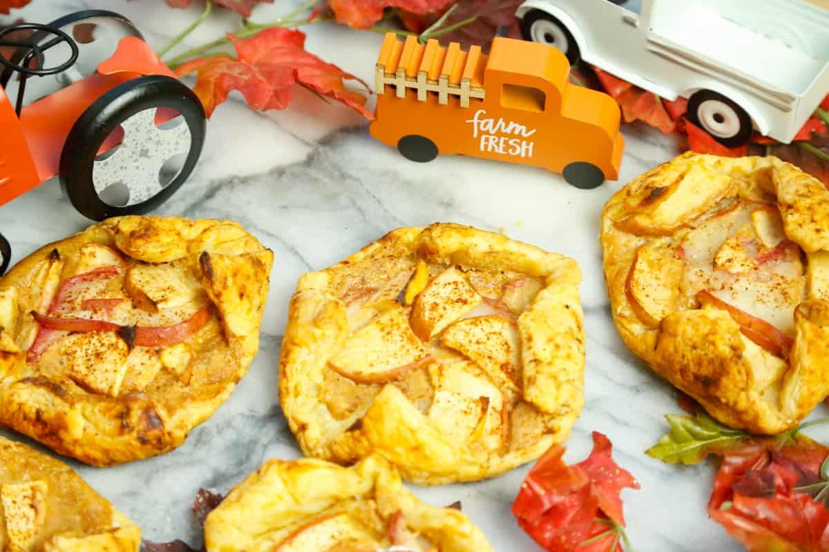 homemade mini apple pies with a farm fresh orange truck, red leaves, on a marble backdrop 