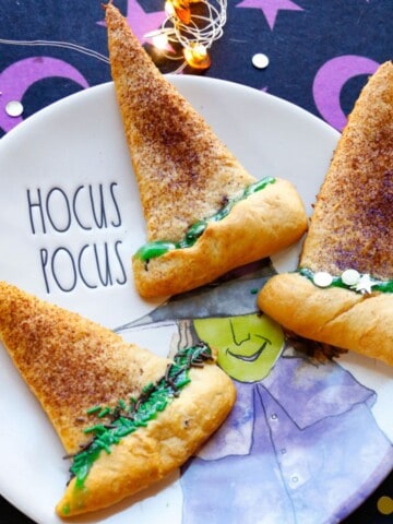 Crescent Witch hats with green frosting on a hocus pocus rae dunn plate with a purple and black background