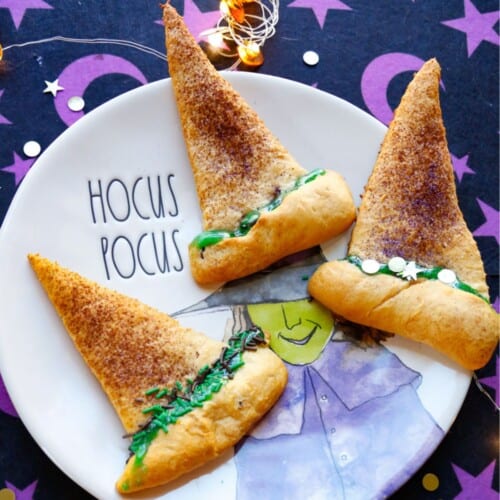 Crescent Witch hats with green frosting on a hocus pocus rae dunn plate with a purple and black background