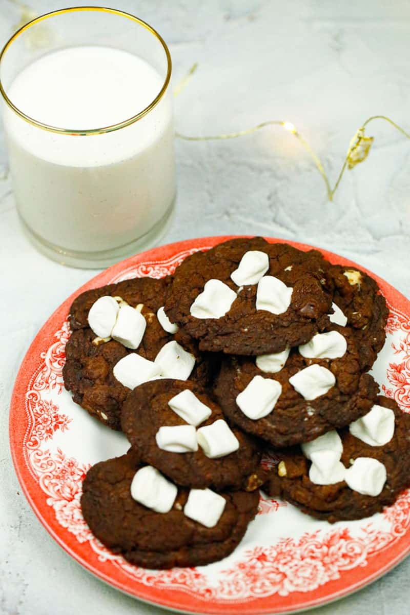 chocolate and marshmallow cookies sitting on a red Christmas plate with a glass of milk 