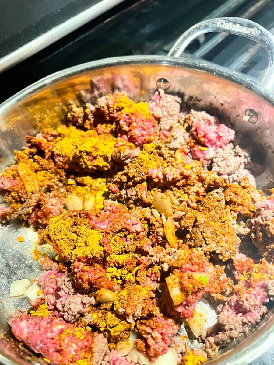 ground beef seasoned with taco seasoning ad chopped onion being sautéed in a pan 