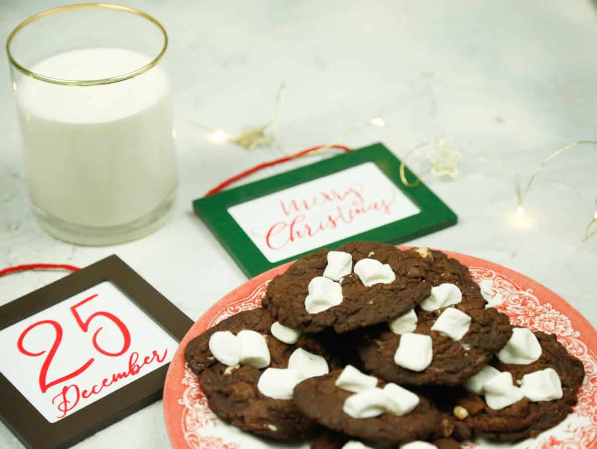 A plate of Christmas cookies with two Christmas signs that says December 25th and Merry Christmas chocolate marshmallow cookies