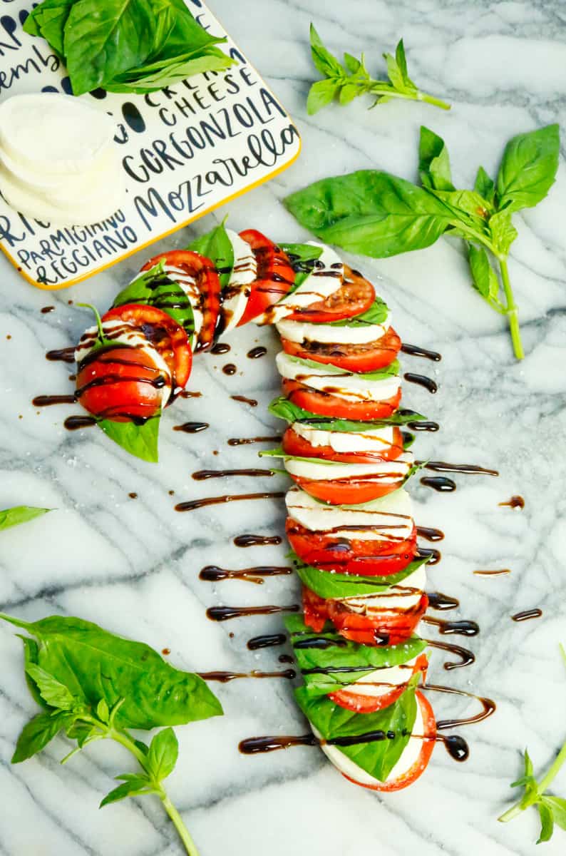 a candy cane appetizer board with mozzarella, basil leaves, and tomato slices drizzled with balsamic vinegar and celtic sea salt 