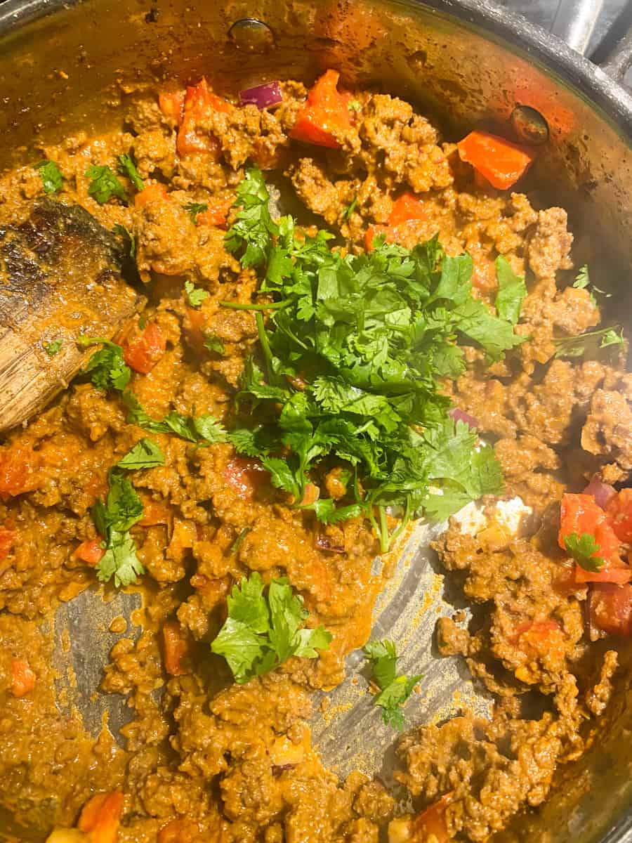 fresh cilantro being added to ground beef in a pan on the stovetop