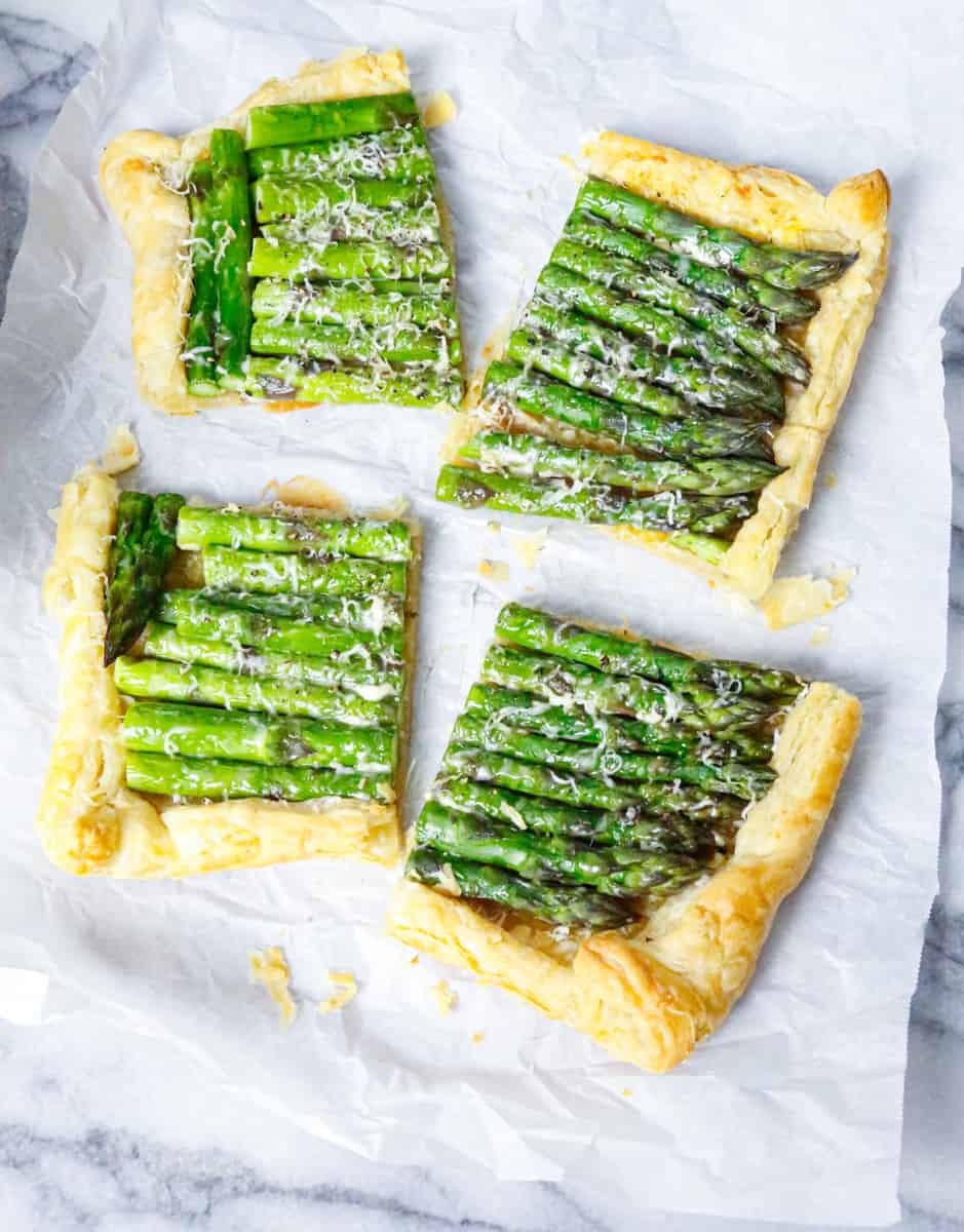 sliced cooked asparagus puff pastry tart on a marble backdrop on parchment paper 