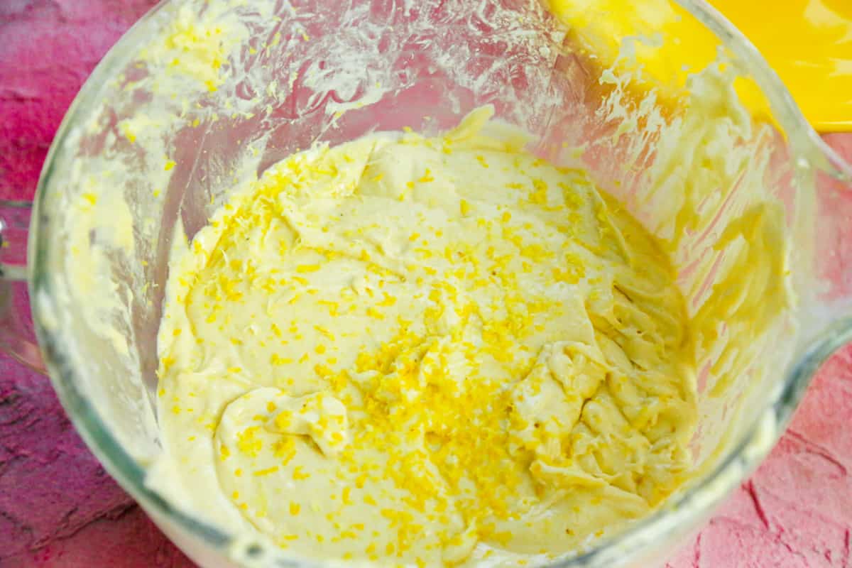 prepared lemon glaze with fresh lemon zest in a mixing bowl on a pink backdrop 