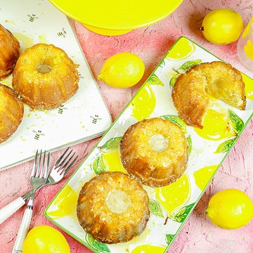mini lemon bundt cakes on a lemon platter next to a yellow cake stand with fresh lemons and silverware
