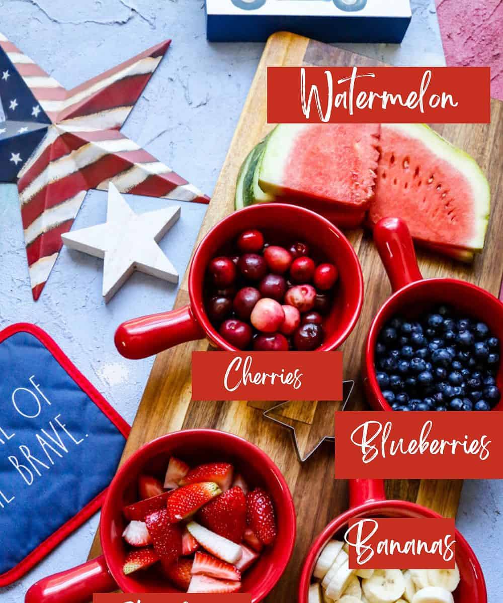 Ingredients for patriotic fruit salad blueberries watermelon strawberries bananas  cherries on a wooden  cutting board 