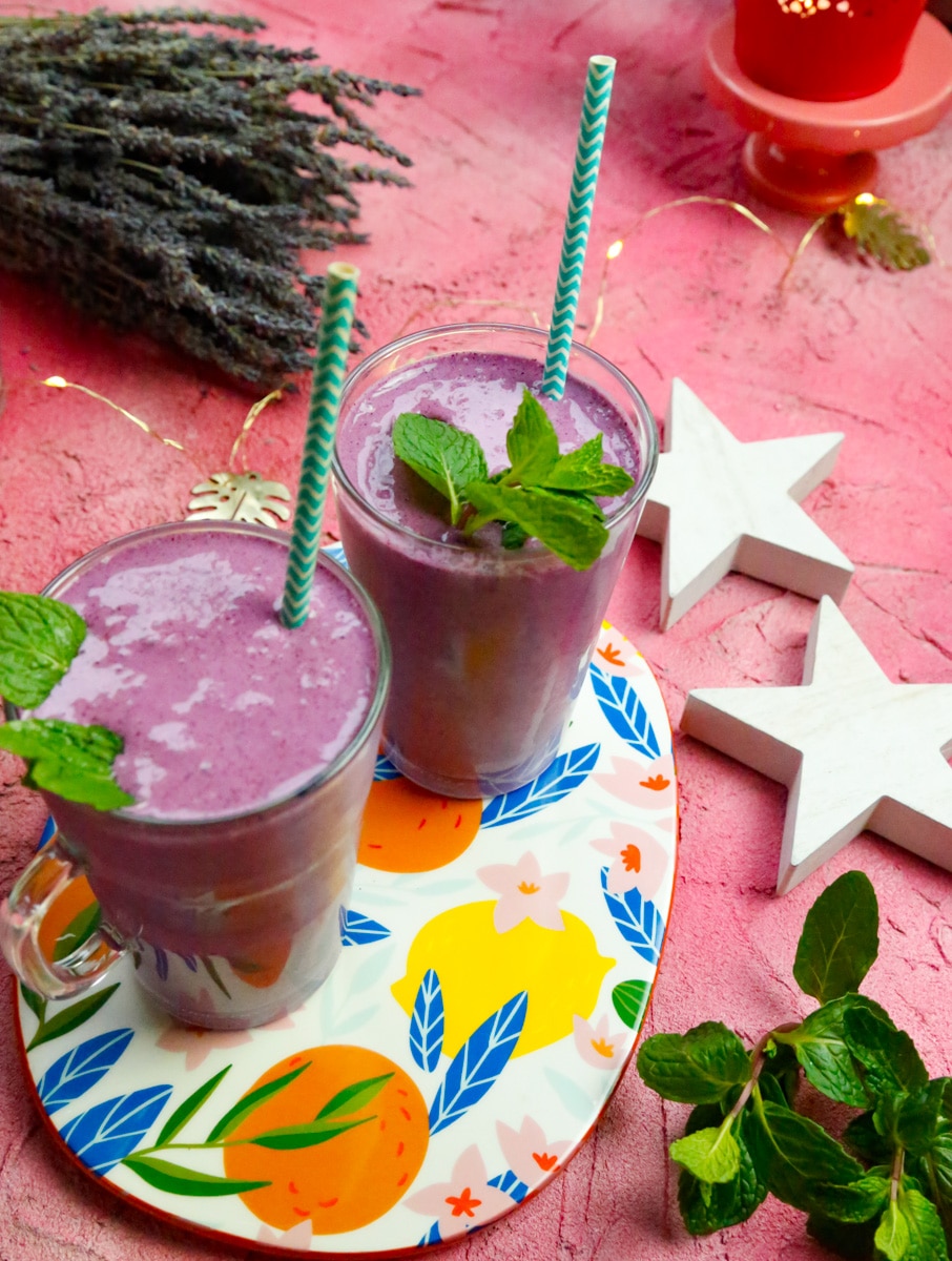two glasses filled with blueberry milkshake with sprigs of fresh mint on top 