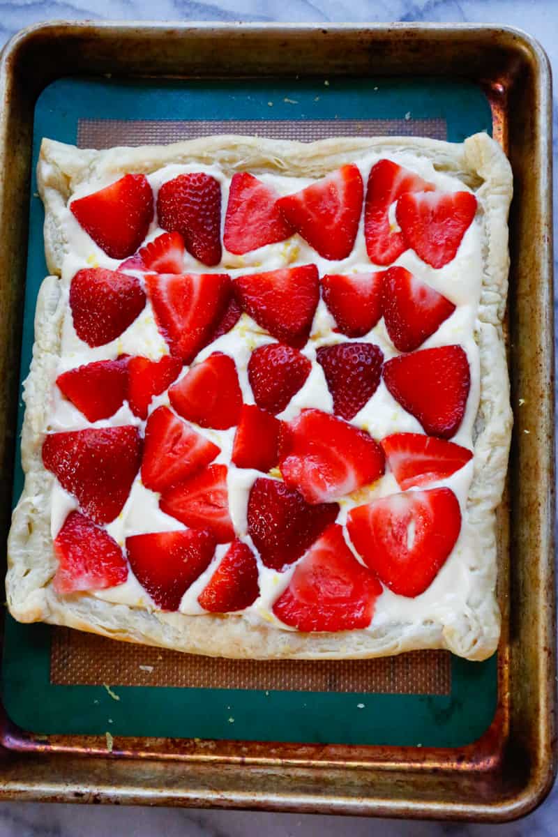 halved strawberries on a cream cheese puff pastry boat on a lined baking sheet 