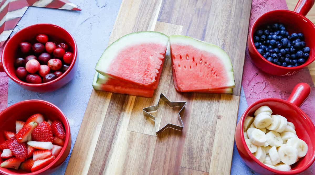 four slices of watermelon and a star shaped cookie cutting on a cutting board 