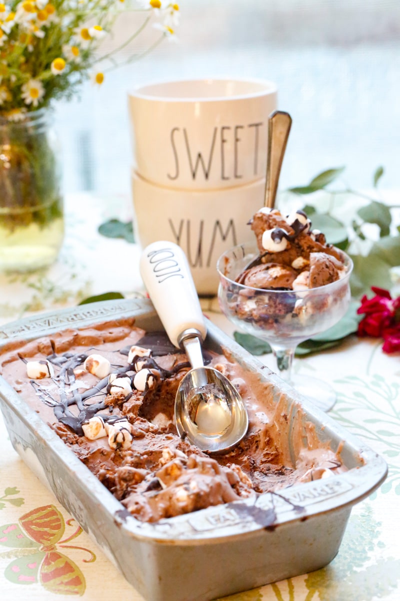 a tray of chocolate marshmallow ice cream with a white ice cream scoop and two white bowls that say sweet and yum on them with dried flowers 